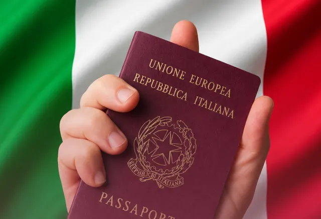 Mão segurando o passaporte italiano diante da bandeira da Itália